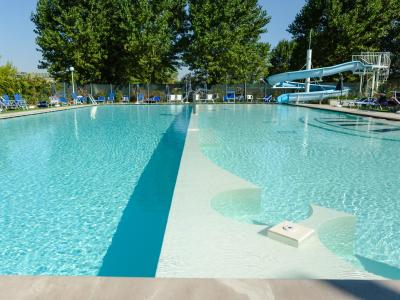 Outdoor pool with slide and loungers, surrounded by trees.