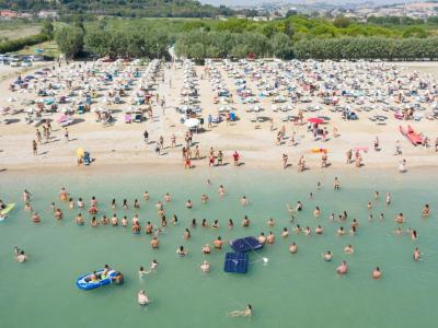 Überfüllter Strand mit Schwimmern und Sonnenschirmen, ruhiges Meer.