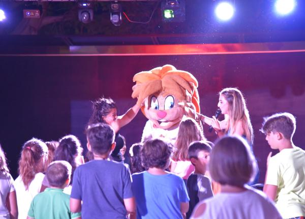 Personaggio mascotte con bambini su un palco illuminato.