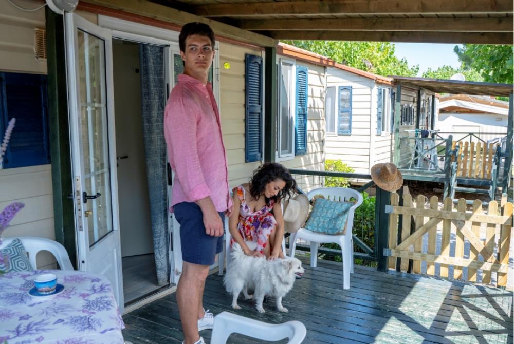 Personnes sur la véranda avec chien, mobil-home en arrière-plan.