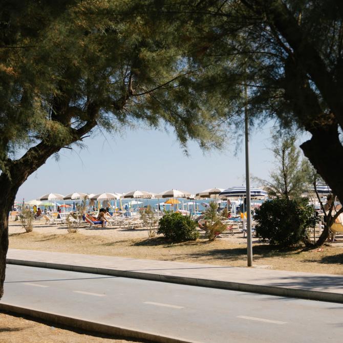 Person radelt am Strand entlang mit Sonnenschirmen.