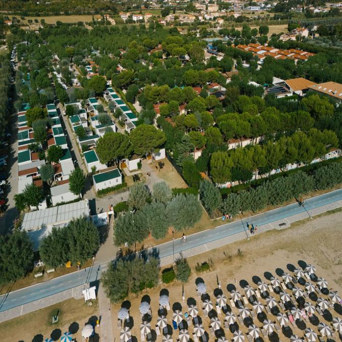 Luftaufnahme eines Campingplatzes in Strandnähe mit Sonnenschirmen.