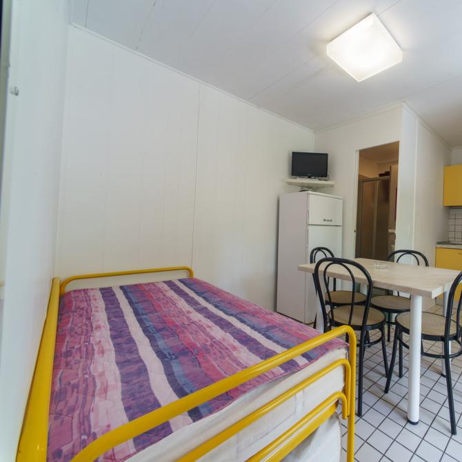 Monolocale con cucina gialla, tavolo, letto e TV.