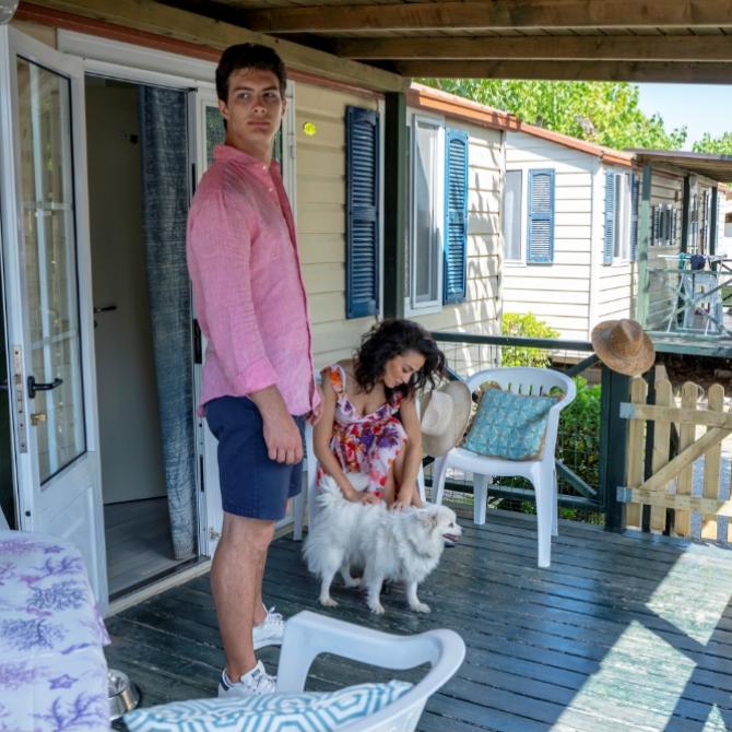 Personnes sur la véranda avec chien, mobil-home en arrière-plan.